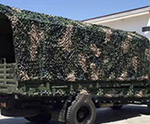 Military vehicle concealed under multi-spectral camouflage netting